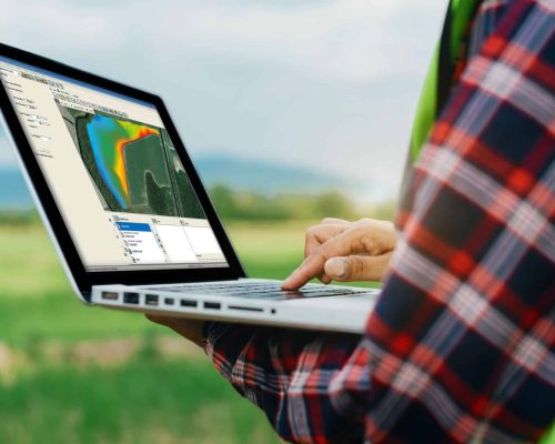 Farmer in a field holding a laptop whilst looking at data in Trimble Ag Software